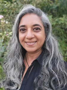 Een warme, persoonlijke foto van Ushadevie Dhanni Bachoe met een natuurlijke groene achtergrond, passend bij haar werk als gids voor innerlijke groei.